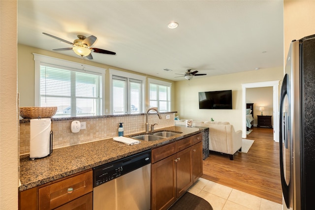 kitchen with light tile patterned floors, decorative backsplash, appliances with stainless steel finishes, a sink, and dark stone countertops