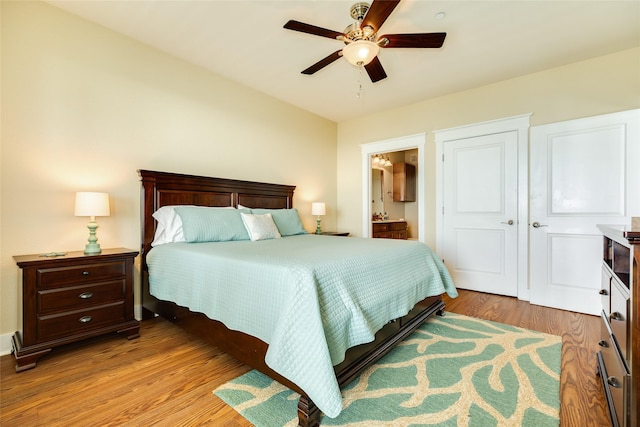 bedroom with ensuite bathroom, light wood finished floors, and a ceiling fan