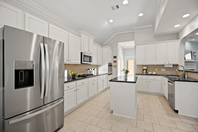 kitchen with dark countertops, appliances with stainless steel finishes, white cabinetry, a sink, and a kitchen island