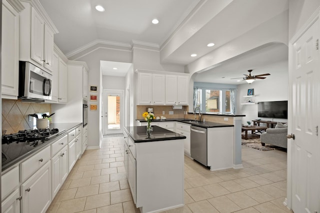 kitchen featuring stainless steel appliances, a peninsula, a sink, a center island, and dark countertops