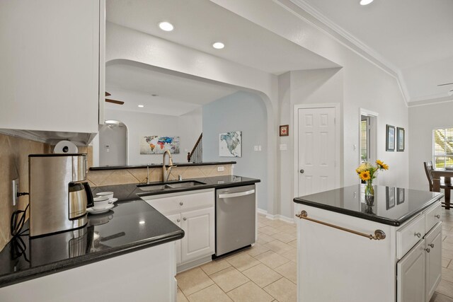 kitchen with arched walkways, dark countertops, stainless steel dishwasher, ornamental molding, and a sink