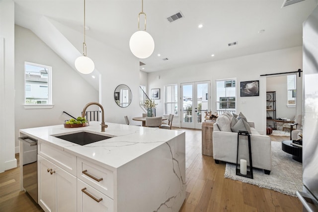 kitchen featuring white cabinets, stainless steel dishwasher, a sink, light wood-style floors, and light stone countertops