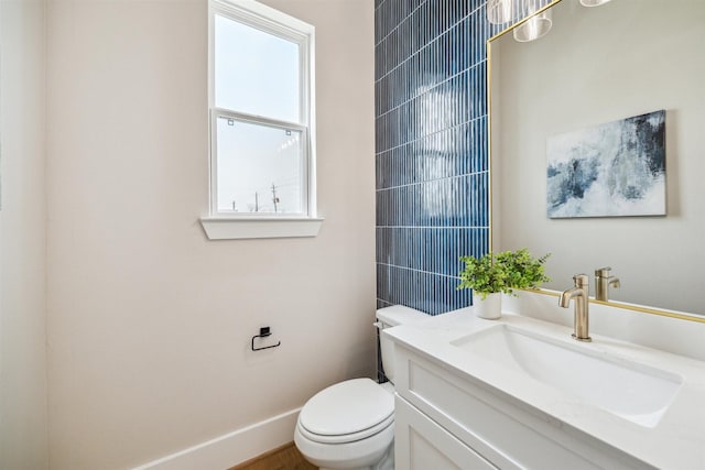 half bath with baseboards, vanity, and toilet
