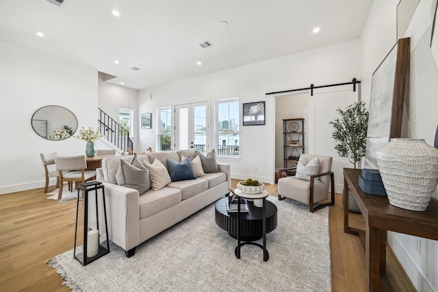 living room featuring light wood-style flooring, a barn door, visible vents, recessed lighting, and stairway