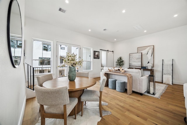 dining area featuring a barn door, light wood-style floors, baseboards, visible vents, and recessed lighting
