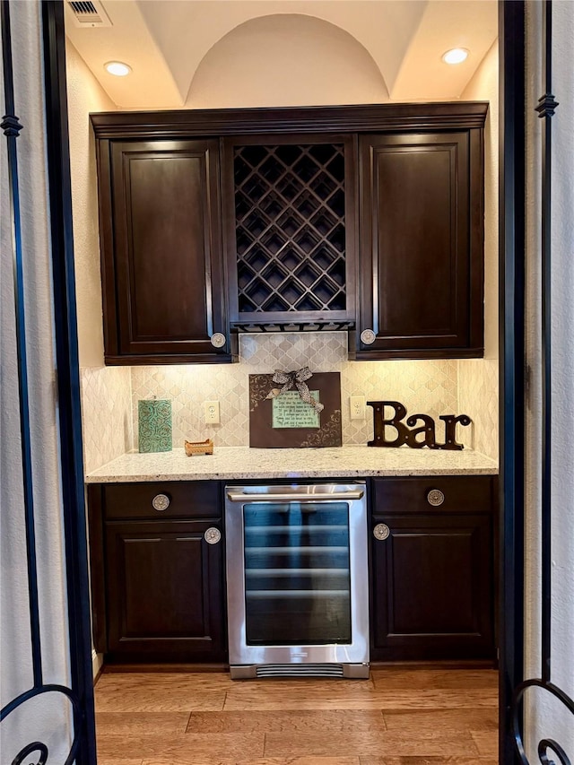 bar with a bar, light wood-style floors, wine cooler, and backsplash