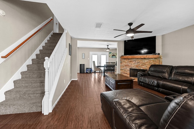 living area featuring a stone fireplace, visible vents, baseboards, stairway, and dark wood-style floors