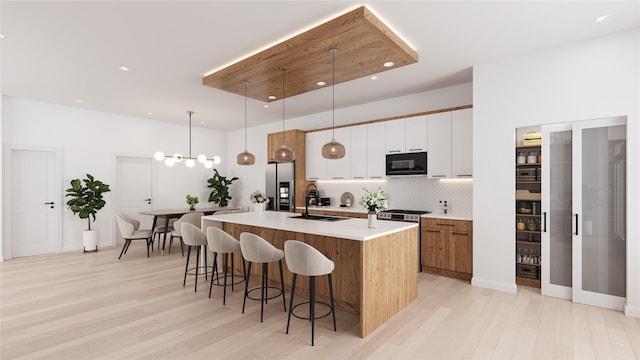 kitchen featuring white cabinets, a sink, an island with sink, black microwave, and stainless steel fridge