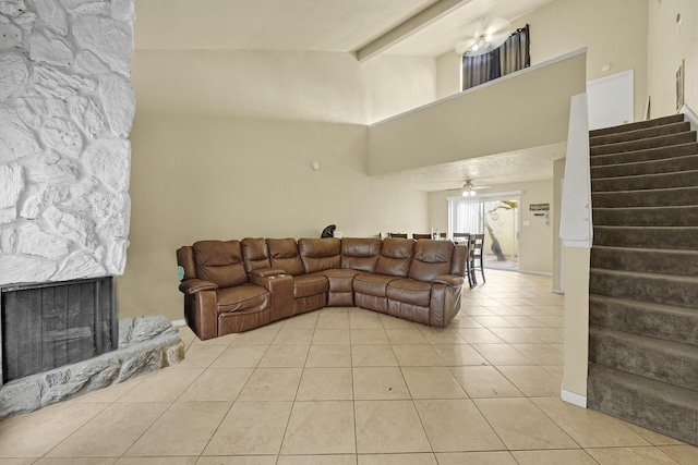 living area featuring ceiling fan, beamed ceiling, stairs, a fireplace, and light tile patterned flooring