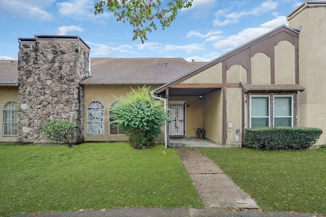 view of property with roof with shingles, a front yard, and stucco siding