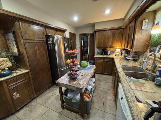 kitchen with freestanding refrigerator, dishwasher, light countertops, a sink, and decorative backsplash