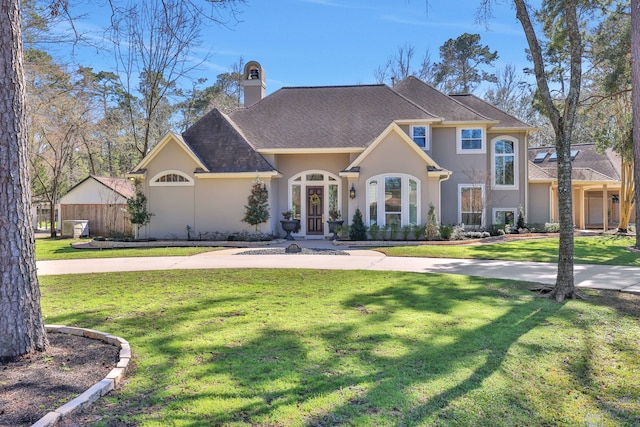 view of front facade featuring a front yard, roof with shingles, a chimney, and stucco siding