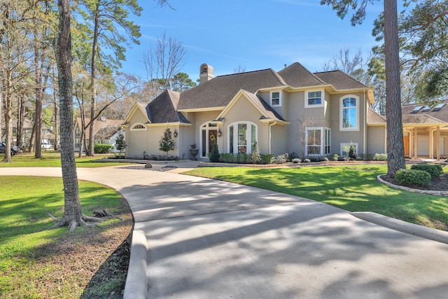 view of front of property with stucco siding, a chimney, concrete driveway, and a front yard