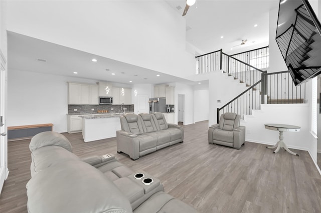 living room featuring light wood finished floors, recessed lighting, a towering ceiling, baseboards, and stairs