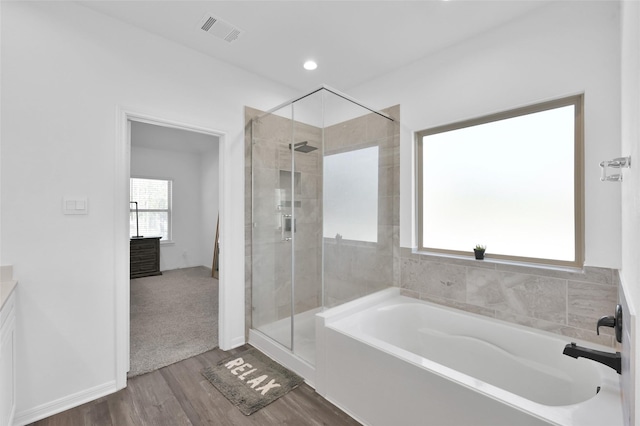 bathroom with wood finished floors, a stall shower, a garden tub, and visible vents