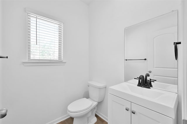 half bathroom featuring wood finished floors, vanity, toilet, and baseboards