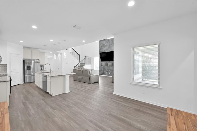 kitchen featuring stainless steel appliances, light wood-style floors, open floor plan, white cabinets, and light stone countertops