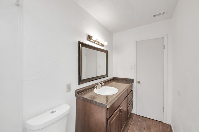 half bathroom featuring toilet, vanity, wood finished floors, and visible vents