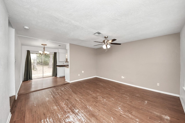 unfurnished living room featuring baseboards, visible vents, dark wood-type flooring, a textured ceiling, and ceiling fan with notable chandelier