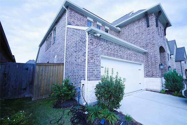 view of property exterior with concrete driveway, brick siding, fence, and an attached garage