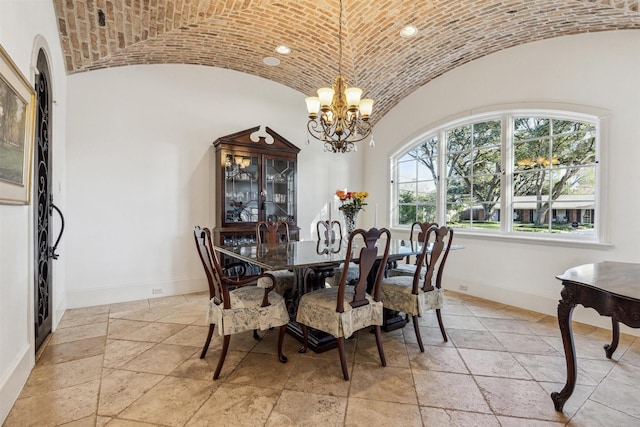 dining space featuring stone tile floors, lofted ceiling, an inviting chandelier, brick ceiling, and baseboards