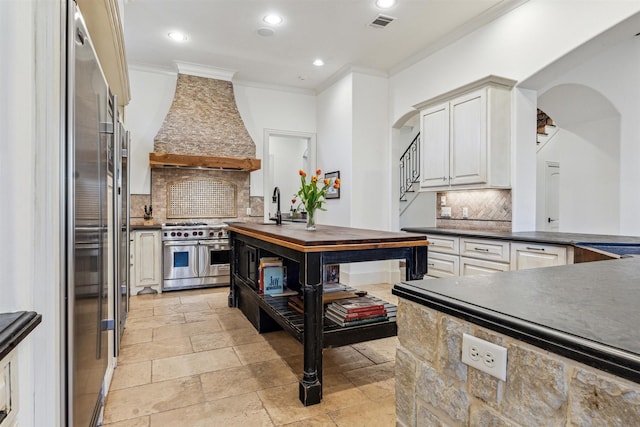 kitchen with arched walkways, range with two ovens, custom range hood, crown molding, and a sink