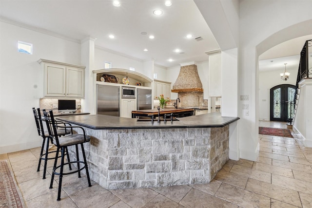 kitchen with dark countertops, a sink, built in appliances, a peninsula, and a kitchen bar