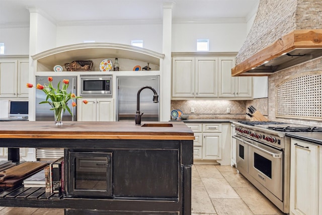 kitchen featuring cream cabinetry, stainless steel appliances, custom range hood, ornamental molding, and wood counters