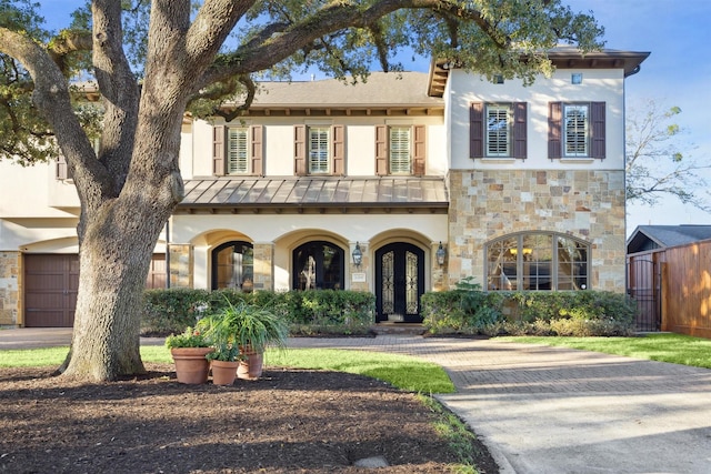 mediterranean / spanish-style house featuring metal roof, stone siding, french doors, stucco siding, and a standing seam roof