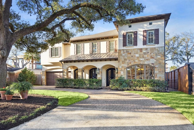 mediterranean / spanish home featuring stone siding, a standing seam roof, fence, decorative driveway, and stucco siding