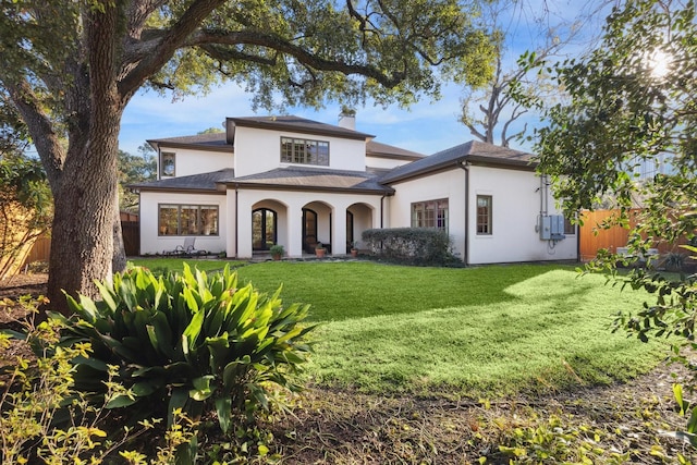 view of front of property with a front yard, fence, a chimney, and stucco siding