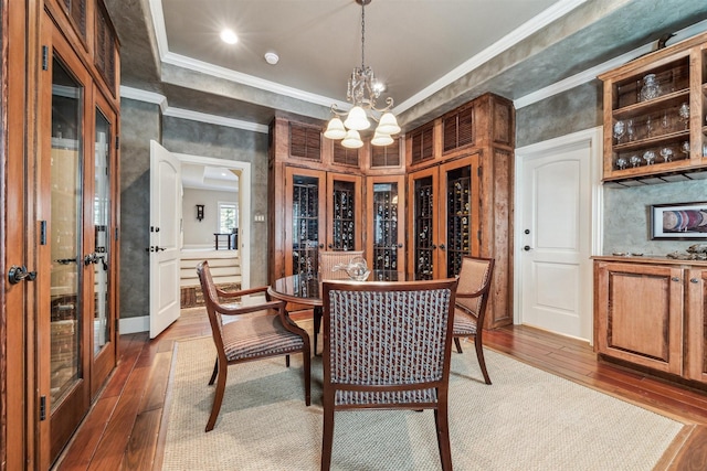 dining room featuring an inviting chandelier, wood-type flooring, ornamental molding, and a raised ceiling