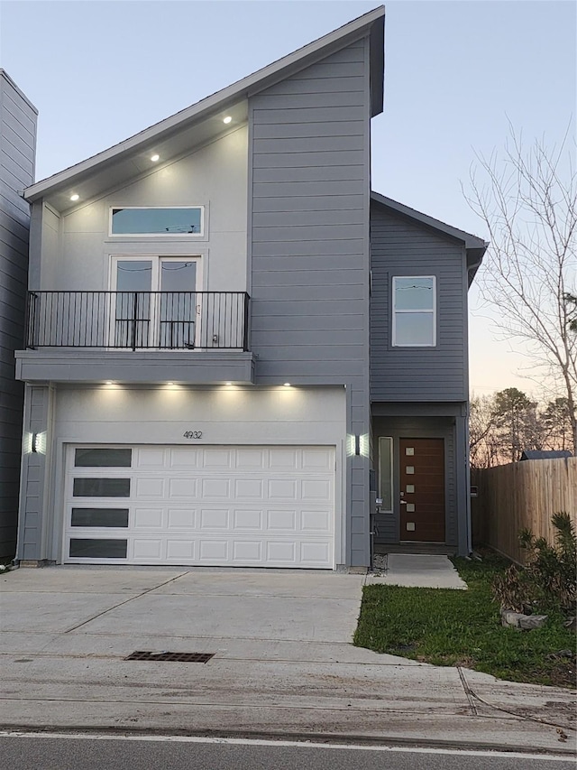 modern home with concrete driveway, fence, a balcony, and a garage