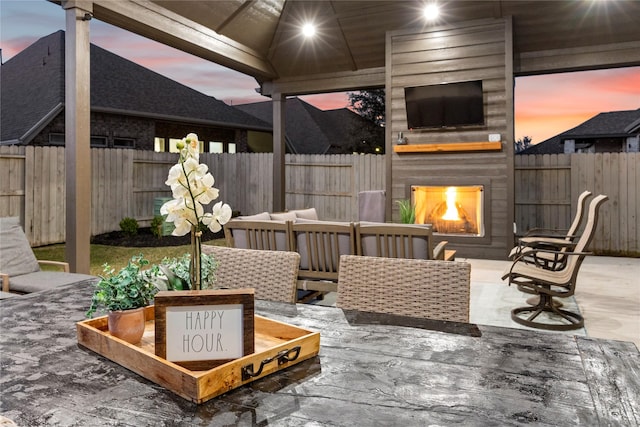 patio terrace at dusk with an outdoor living space with a fireplace and a fenced backyard