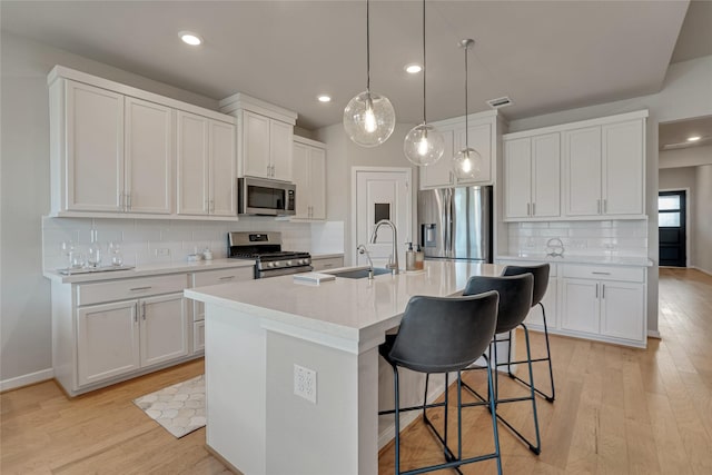 kitchen with stainless steel appliances, light countertops, a center island with sink, and white cabinetry