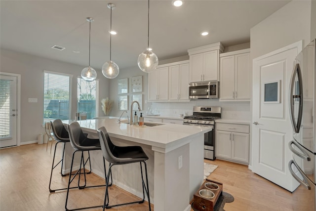 kitchen featuring light countertops, appliances with stainless steel finishes, white cabinets, a sink, and an island with sink