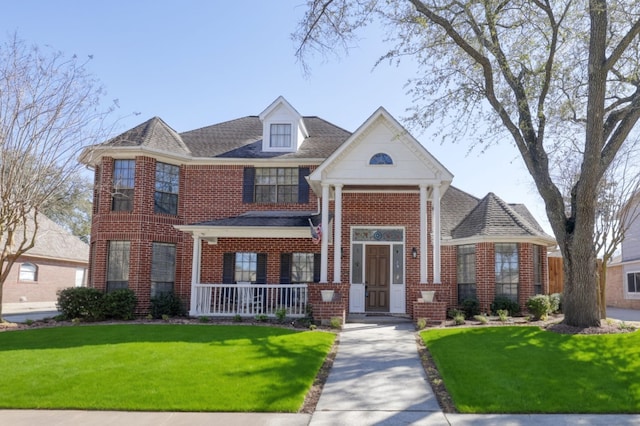 view of front of house featuring covered porch, brick siding, a front yard, and a shingled roof