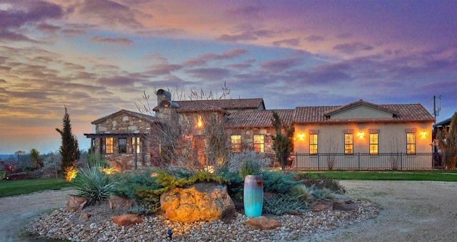 view of front of house featuring a chimney, stone siding, fence, and a tiled roof