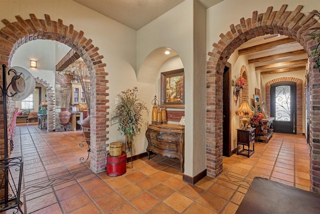 foyer entrance with baseboards, visible vents, arched walkways, beamed ceiling, and tile patterned flooring