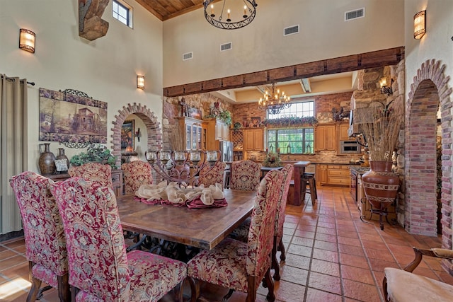 dining room featuring a towering ceiling, an inviting chandelier, visible vents, and arched walkways