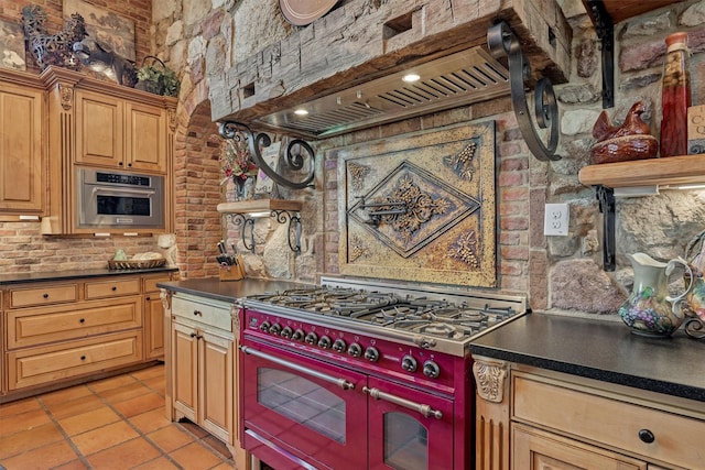 kitchen featuring light tile patterned flooring, brick wall, stainless steel appliances, custom exhaust hood, and dark countertops