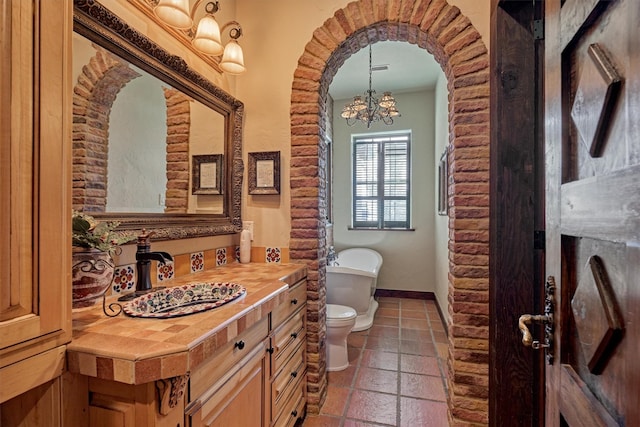 full bathroom featuring baseboards, toilet, an inviting chandelier, a freestanding bath, and vanity