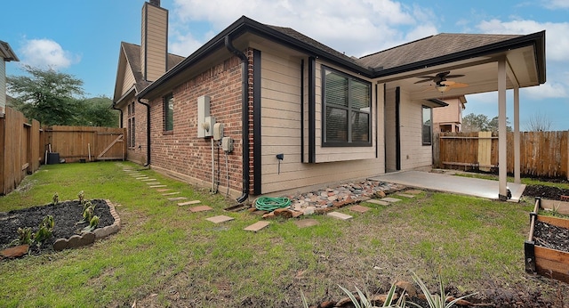 view of side of home featuring a yard, brick siding, a fenced backyard, and a ceiling fan