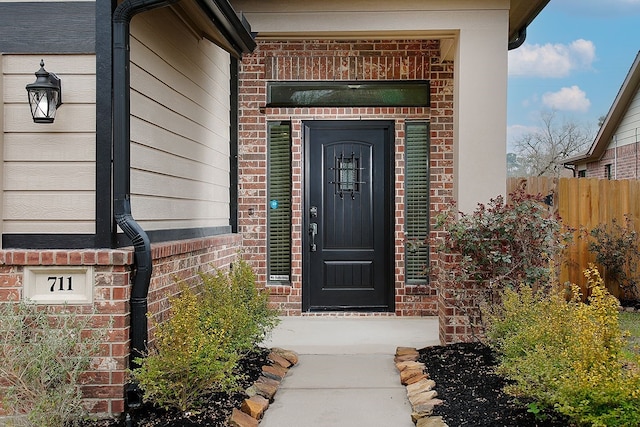 view of exterior entry with brick siding and fence