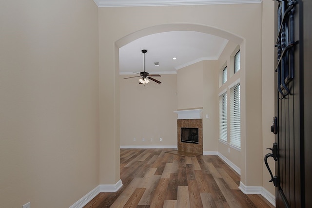 unfurnished living room with ceiling fan, a fireplace, wood finished floors, baseboards, and ornamental molding