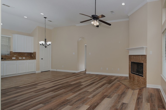 unfurnished living room with baseboards, arched walkways, visible vents, wood finished floors, and a fireplace