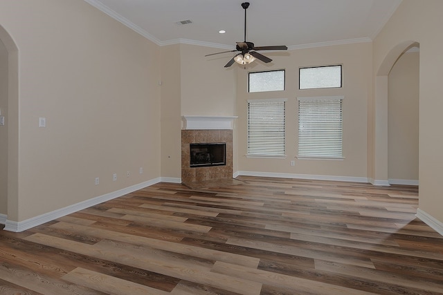 unfurnished living room with arched walkways, visible vents, wood finished floors, a tile fireplace, and baseboards