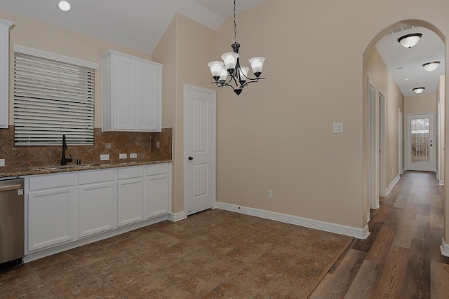 kitchen with decorative backsplash, dark stone counters, a sink, white cabinetry, and stainless steel dishwasher