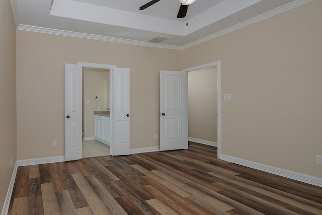 unfurnished bedroom with dark wood-style floors, baseboards, a raised ceiling, and ensuite bathroom