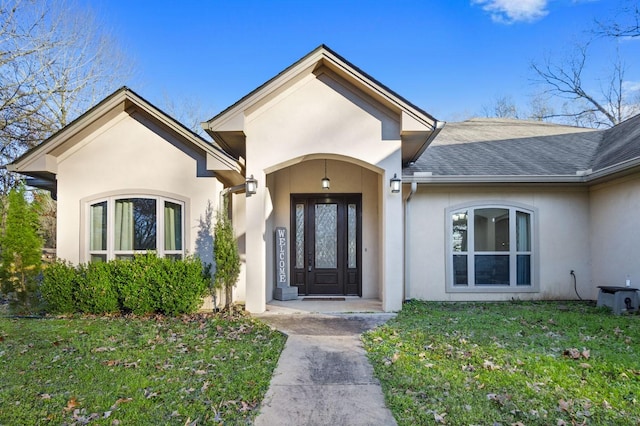 doorway to property with a yard, roof with shingles, and stucco siding